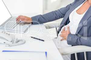 Pregnant businesswoman touching her belly while typing on laptop