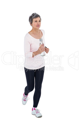 Mature woman holding bottle while jogging