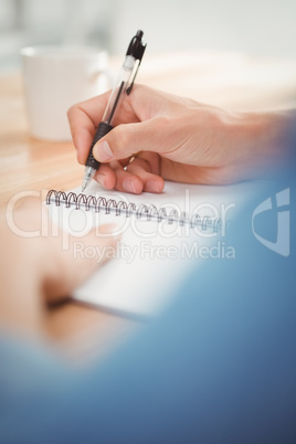 Businessman writing on spiral table at desk