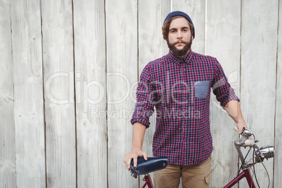 Hipster with bicycle against fence