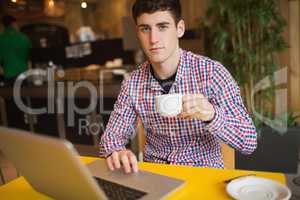 Portrait of young man with coffee using laptop