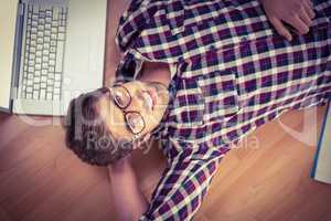 Happy hipster wearing eye glasses lying on hardwood floor