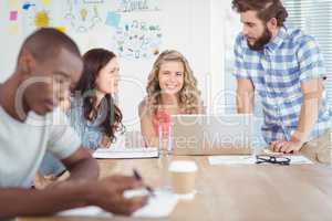 Portrait of smiling woman with coworkers working at desk