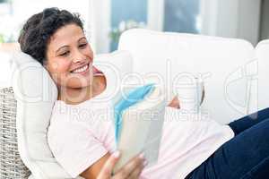 Pregnant woman reading book while holding coffee cup