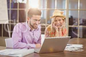 Business woman wearing hat sitting by male colleague