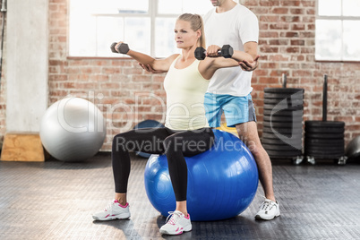 Male trainer helping young woman with the dumbbells