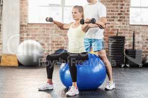 Male trainer helping young woman with the dumbbells