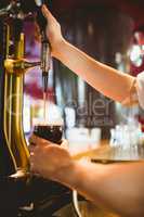 Bartender holding glass below beer dispenser tap