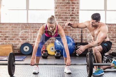 Woman lifting barbell with her trainer