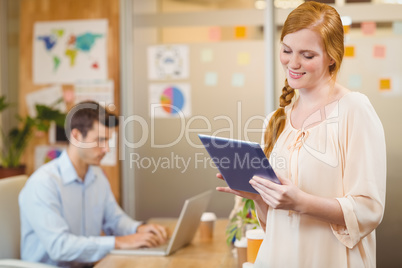 Businesswoman holding digital tablet with male colleague working