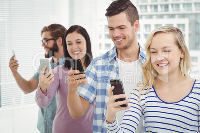 Smiling business people using smartphones while standing in row