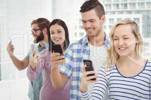 Smiling business people using smartphones while standing in row