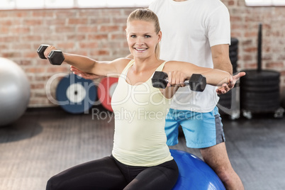 Male trainer helping young woman with the dumbbells