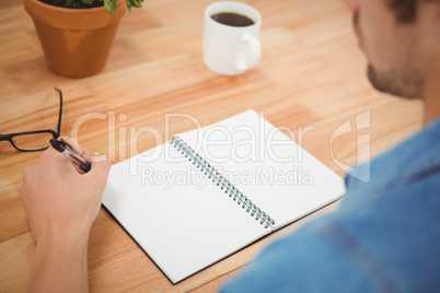 Hipster holding pen with spiral book and coffee on table