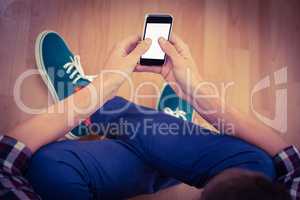 Hipster using smartphone while sitting on hardwood floor