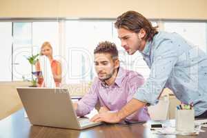 Businessmen working on laptop with female colleague in backgroun