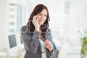 Happy businesswoman holding eyeglasses talking on smartphone