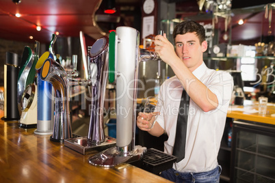 Bartender holding glass standing in front of beer dispenser