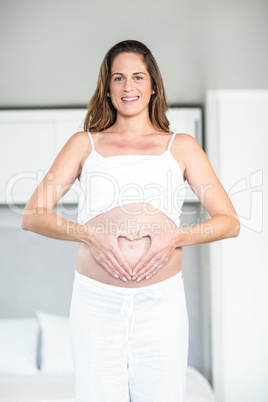 Portrait of happy woman making heart on abdomen