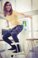 Happy hipster standing on chair by desk in office