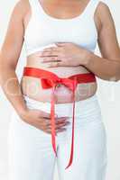 Midsection of pregnant woman with a red ribbon around her bump