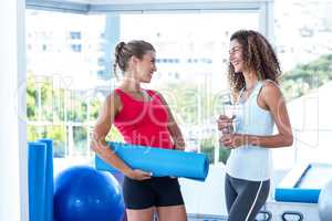 Women looking at each other while holding exercise mat and water