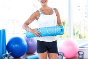 Midsection of woman smiling while holding yoga mat