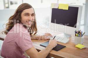 Hipster smiling while using graphics tablet at computer desk