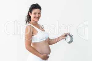Smiling pregnant woman holding alarm clock