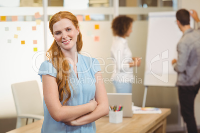 Smiling businesswoman with arm crossed with colleagues in backgr