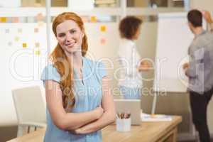 Smiling businesswoman with arm crossed with colleagues in backgr