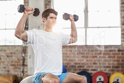 Man sitting on a bossu lifting dumbbells