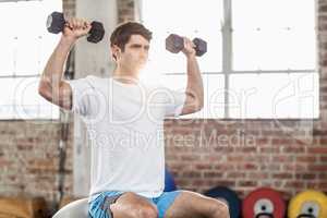 Man sitting on a bossu lifting dumbbells