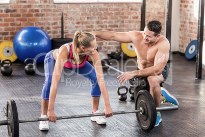 Woman lifting barbell with her trainer