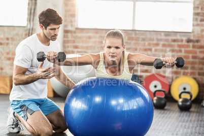 Male trainer helping young woman with the dumbbells