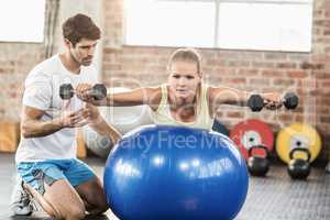 Male trainer helping young woman with the dumbbells