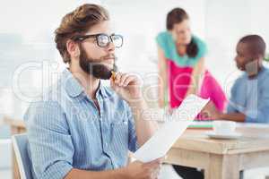 Thoughtful man wearing eyeglasses and holding paper