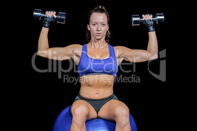 Portrait of woman lifting dumbbells while sitting on exercise ba