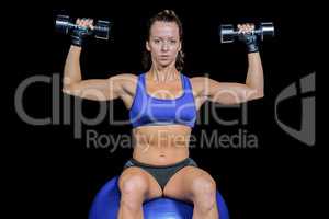 Portrait of woman lifting dumbbells while sitting on exercise ba