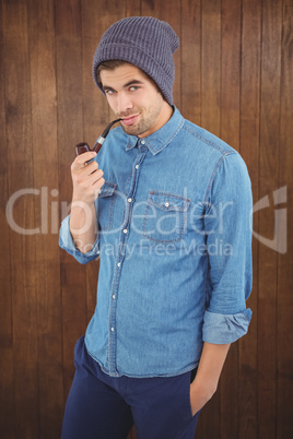 Confident hipster wearing knitted hat smoking pipe