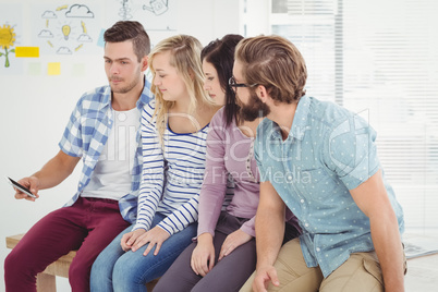 Man holding mobile phone while sitting at desk with coworkers