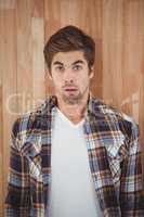 Portrait of surprised hipster standing against wooden wall