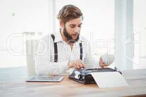Hipster holding coffee working on typewriter
