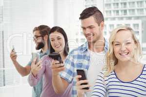 Happy business people using smartphones while standing in row