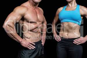 Midsection of muscular man and woman with hands on hip