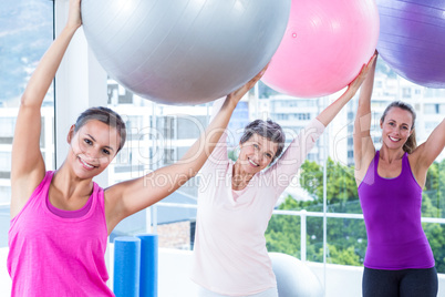 Portrait of happy women holding exercise balls with arms raised