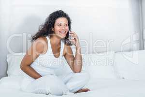 Beautiful woman talking on mobile phone while sitting on bed