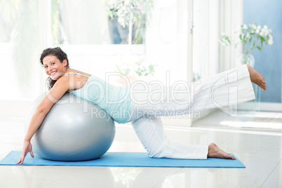 Smiling pregnant woman stretching with exercise ball