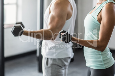 Mid section of couple exercising with dumbbells in gym