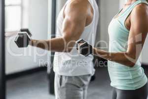 Mid section of couple exercising with dumbbells in gym